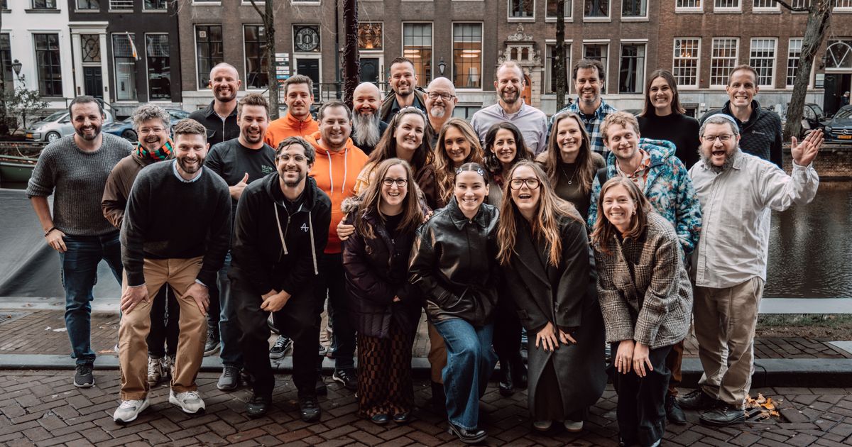 Group of marketing analytics professionals posing outdoors beside a canal, smiling in casual attire with brick townhouses in the background, captured during a meetup for industry insights.