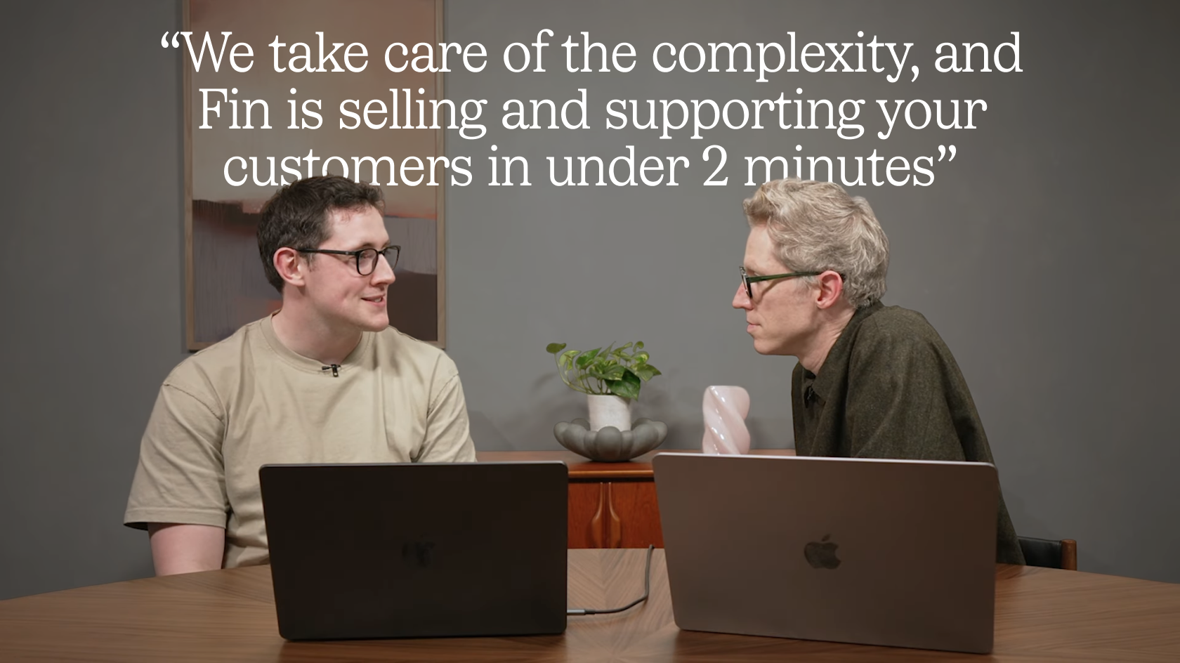 Two colleagues in a studio sit at a wooden table with laptops during a Fin Product Updates discussion; an overlaid quote highlights selling and supporting customers in under two minutes.