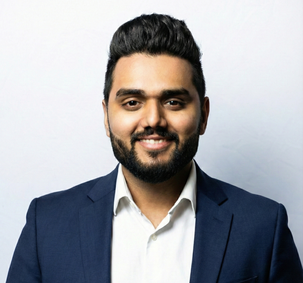 Professional studio headshot of a smiling man in a navy blazer and white dress shirt against a light background, conveying confidence and approachability for corporate leadership profiles.