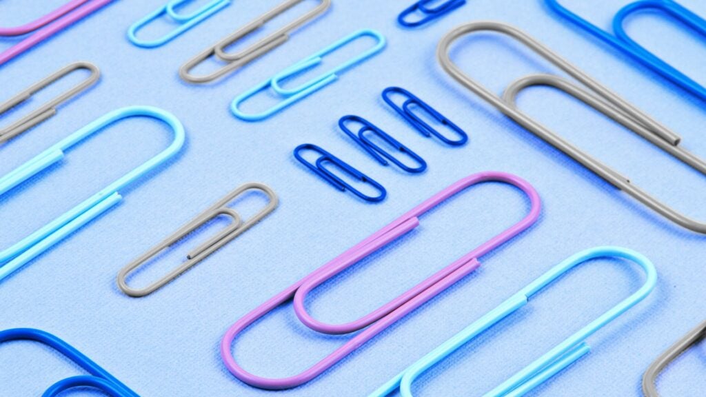 Assorted blue, pink, and gray paper clips scattered across a light blue surface.